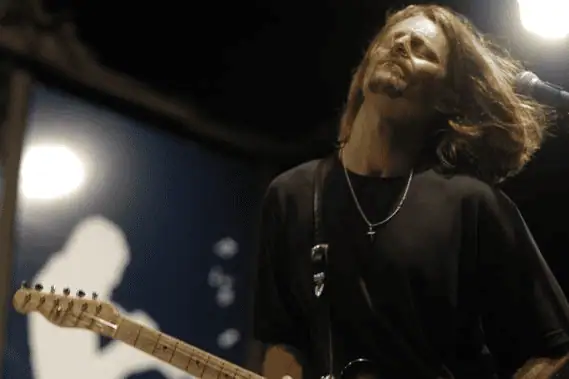 Guitarist performing passionately onstage with dramatic lighting.