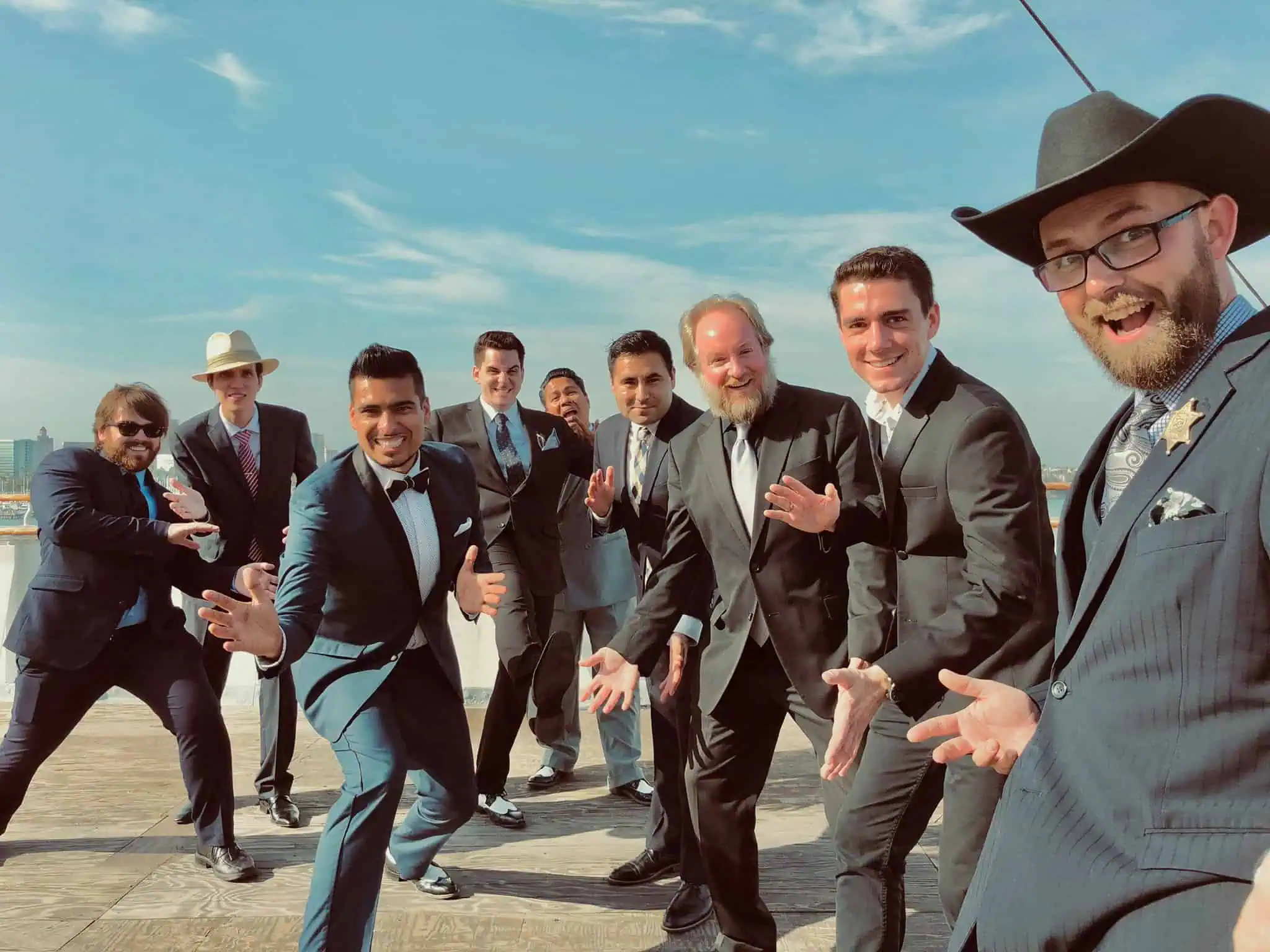 Group of men dressed in suits posing playfully outdoors on a sunny day.