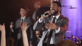 Male performer singing to an excited crowd with fellow vocalists behind him.