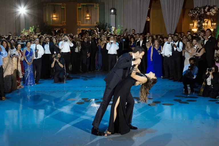 A well-dressed couple sharing a dramatic dance dip on the ballroom floor while guests gather around and cheer.