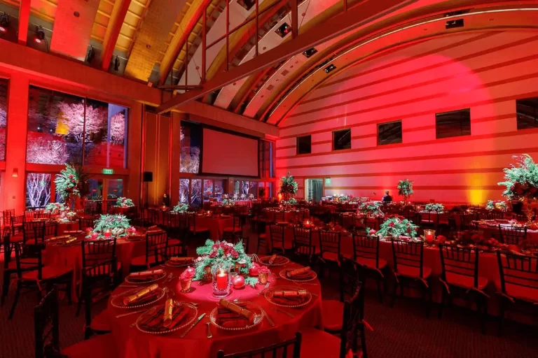 A festive event space decorated in red lighting with round tables, floral centerpieces, and elegant holiday-inspired décor.