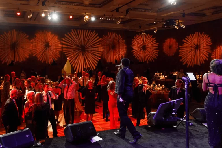 Live performers on stage energizing a ballroom crowd as warm patterned lighting fills the room during an evening celebration.