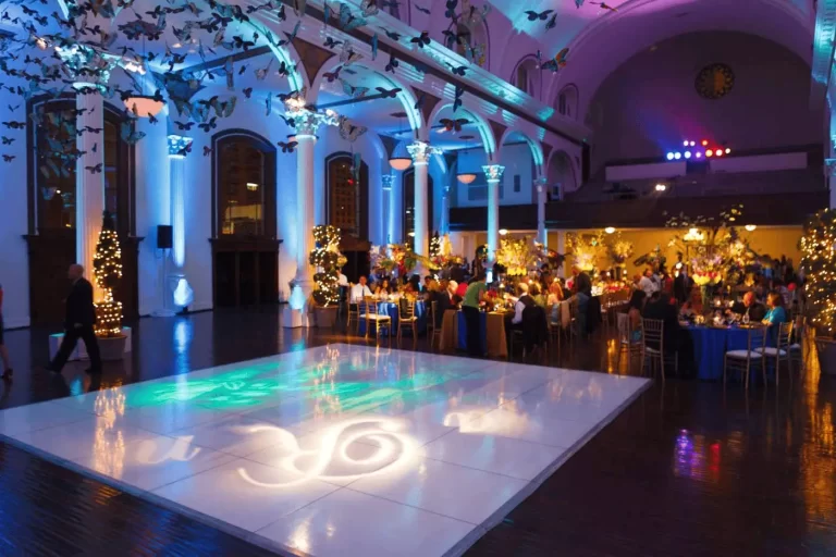 Elegant event hall with a glowing dance floor, dramatic uplighting, and butterfly-themed ceiling décor during an evening celebration.