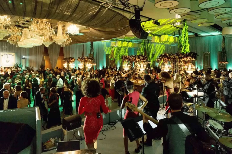 Live band performing at an upscale gala with chandeliers, floral décor, and guests dancing under dramatic green lighting.