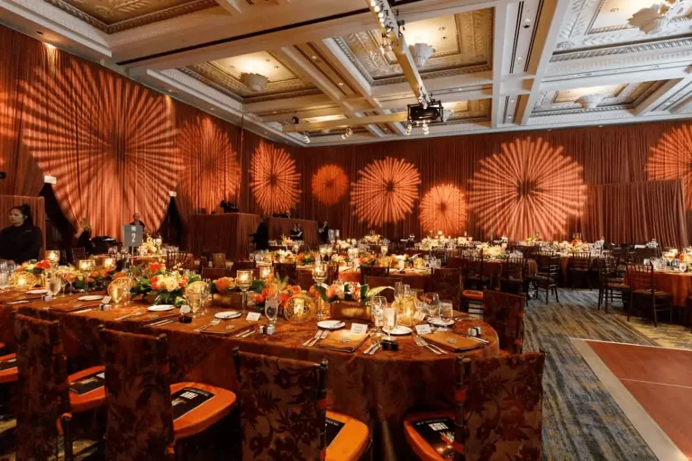 Elegant banquet hall decorated with warm amber lighting, floral centerpieces, and round tables set for a formal event.