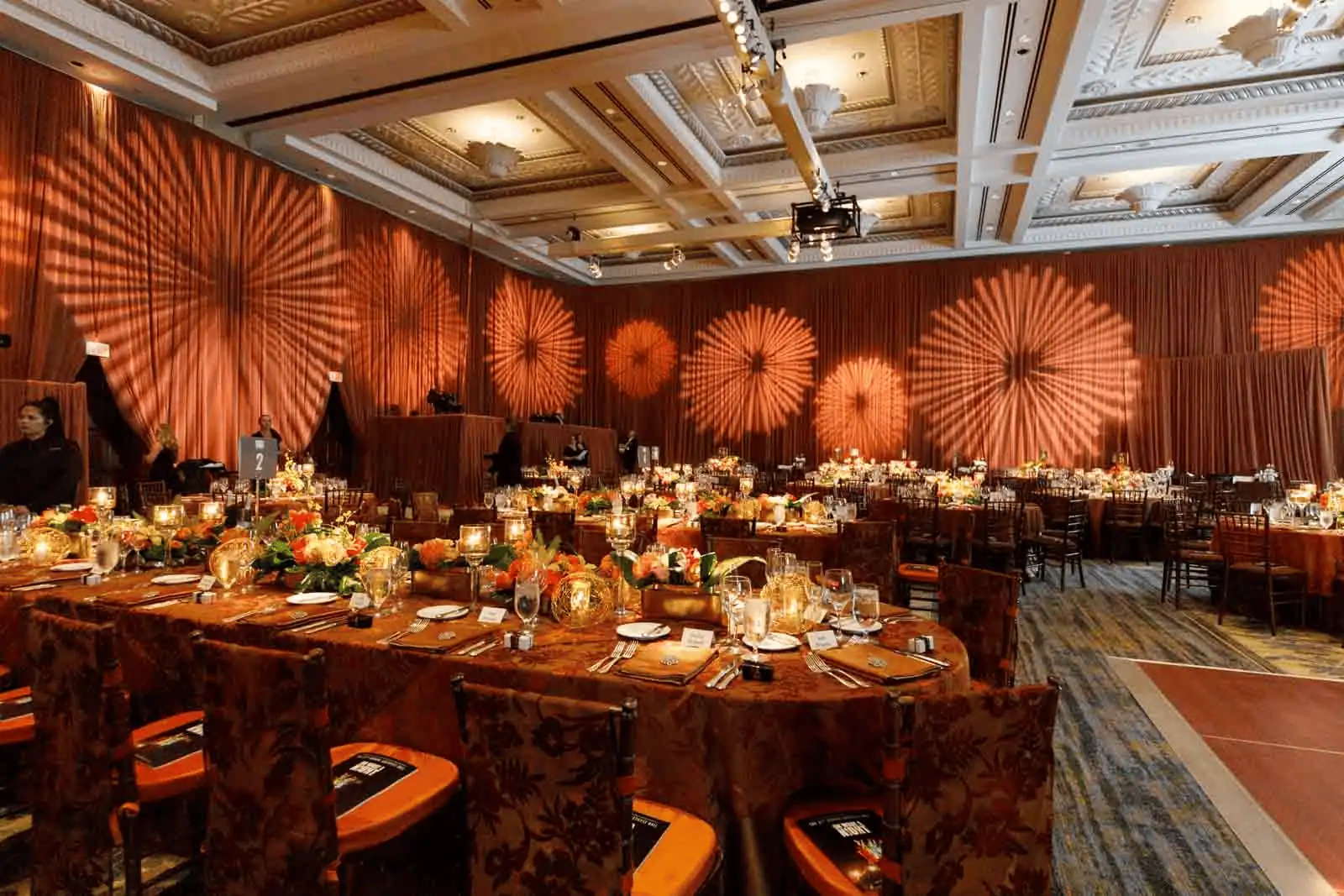 Elegant banquet hall decorated with warm amber lighting, floral centerpieces, and round tables set for a formal event.